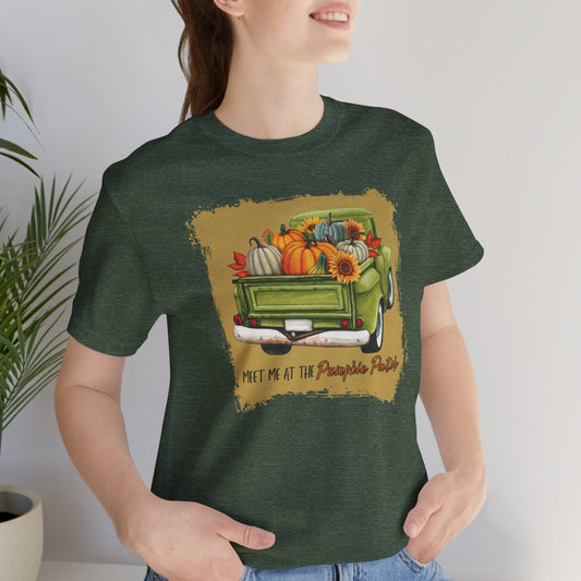 Person wearing a green t-shirt with a graphic of a truck and pumpkins, sitting indoors.