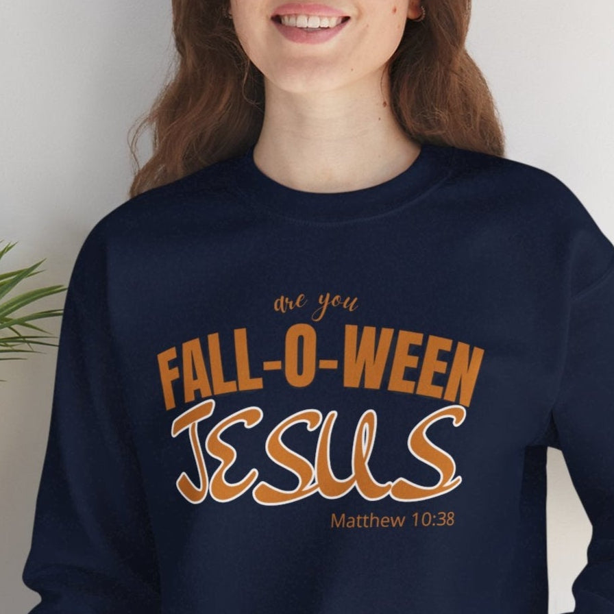 Person wearing a navy sweatshirt with 'Fall-o-ween Jesus' text, sitting against a white wall with a plant.