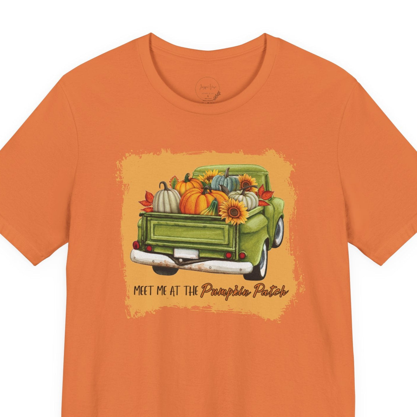 Orange t-shirt with a graphic of a green truck carrying pumpkins and sunflowers, on a white background.