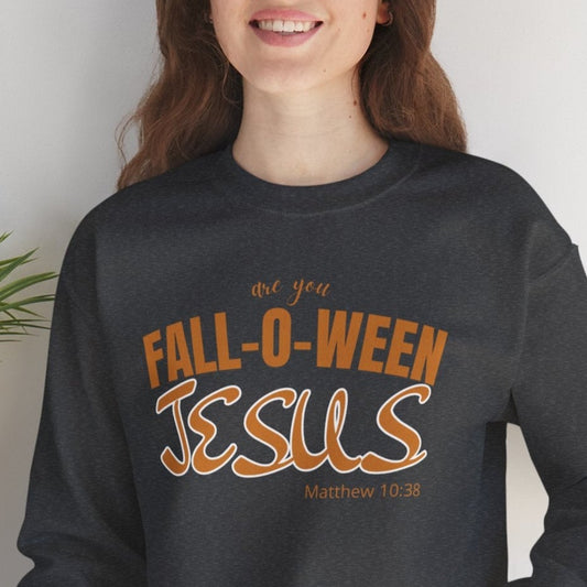 Person wearing a black sweatshirt with 'Fall-o-ween Jesus' text, sitting on a white surface with a plant in the background.