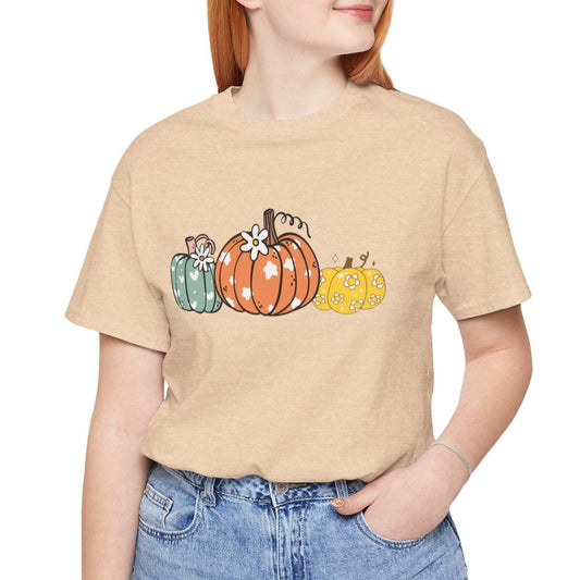 Person wearing a beige t-shirt with pumpkin design and blue jeans on a white background