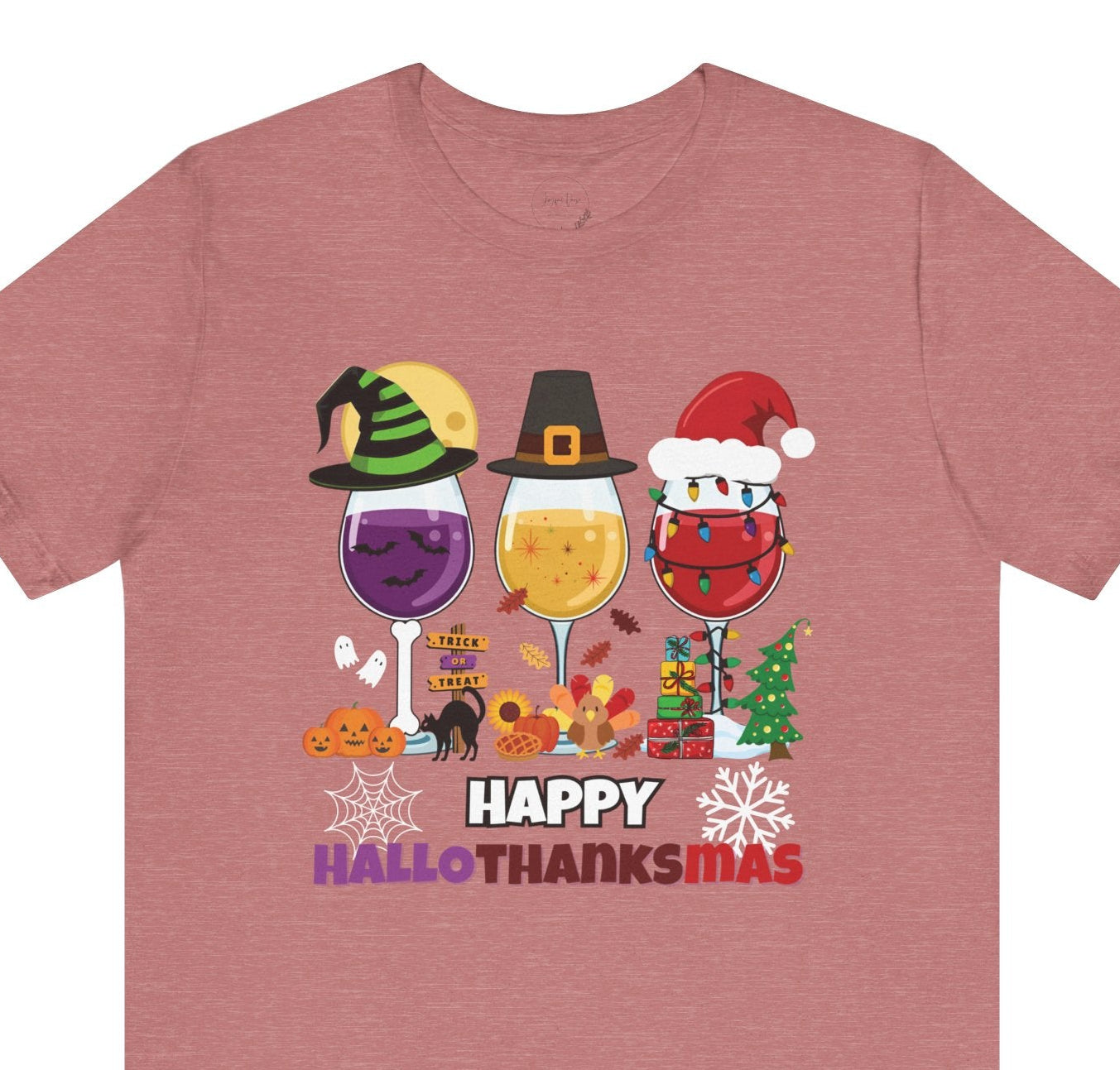 Rose colored t-shirt with 'Happy Hallothanksmas' design featuring wine glasses and holiday elements on a white background.