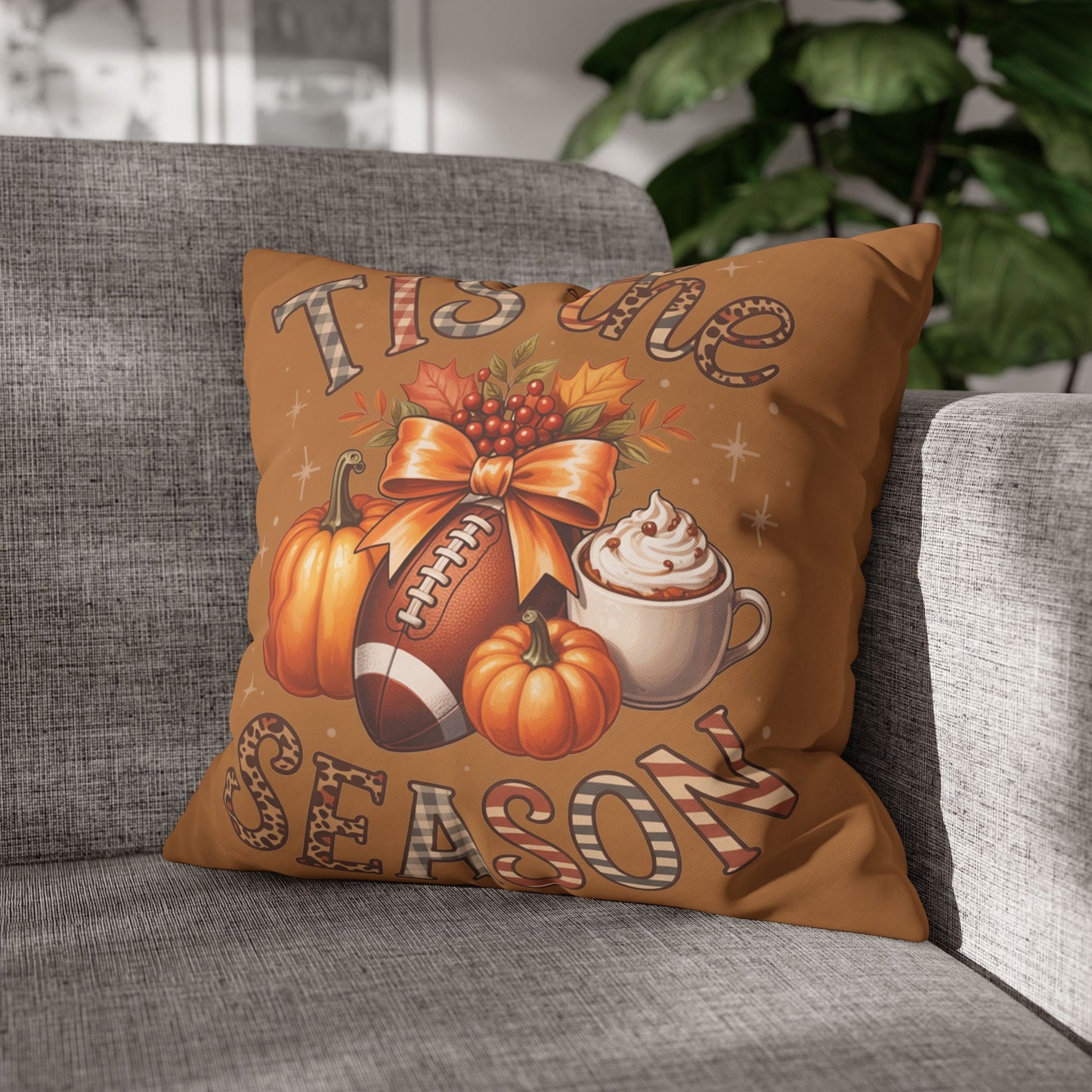 Decorative pillowcase with autumn-themed design featuring pumpkins, a football, and a coffee cup on a gray couch.