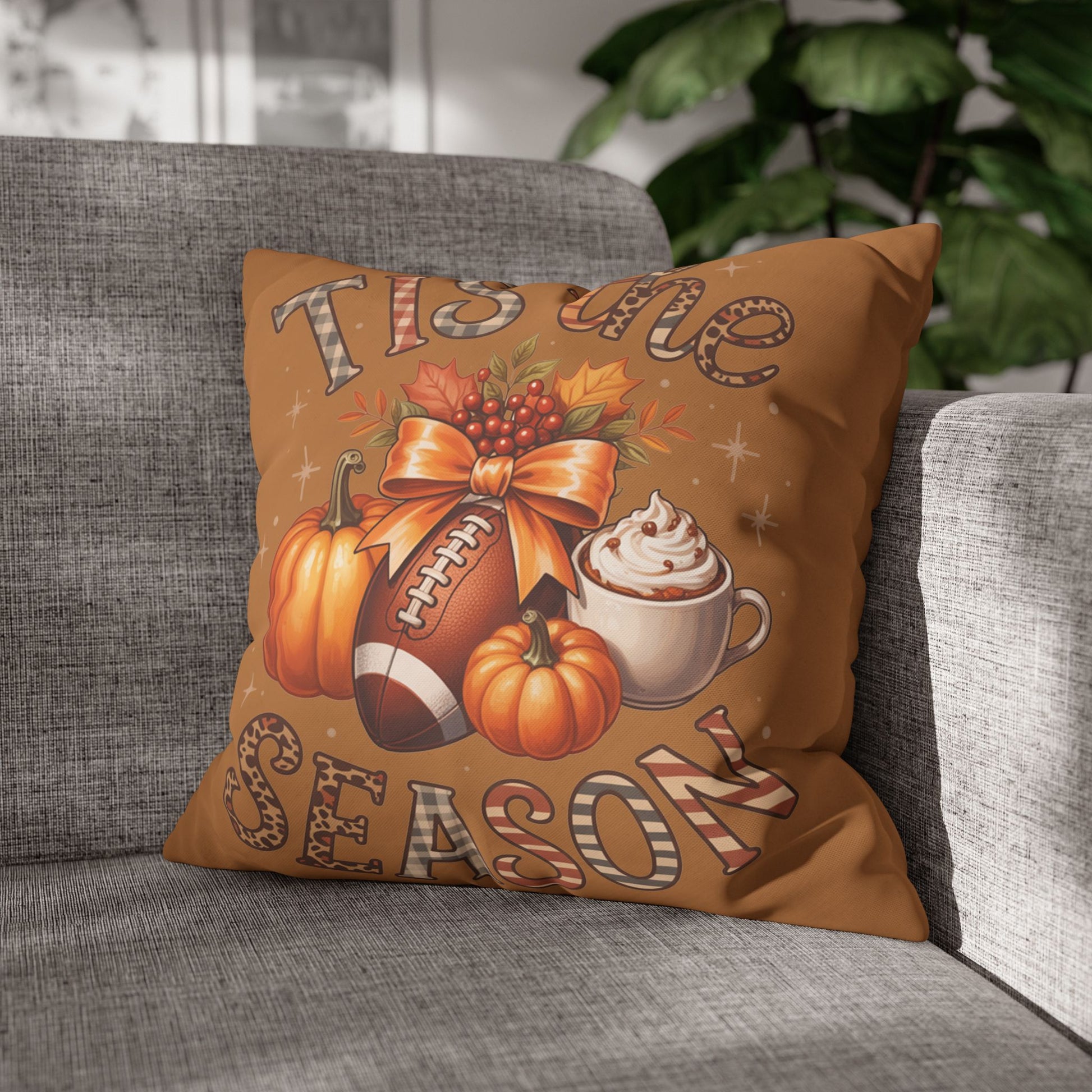 Decorative pillowcase with autumn-themed design featuring pumpkins, a football, and a coffee cup on a gray couch.