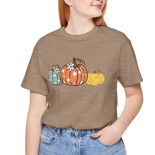 Person wearing a brown t-shirt with colorful pumpkins and blue jeans on a white background