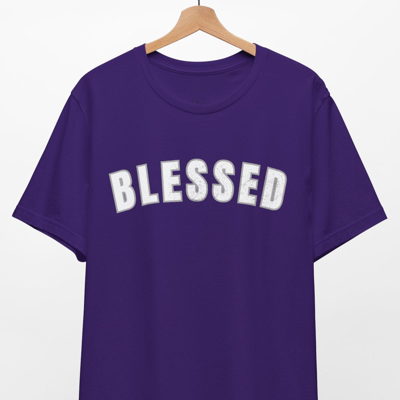 Purple t-shirt with 'BLESSED' text on a hanger against a white background