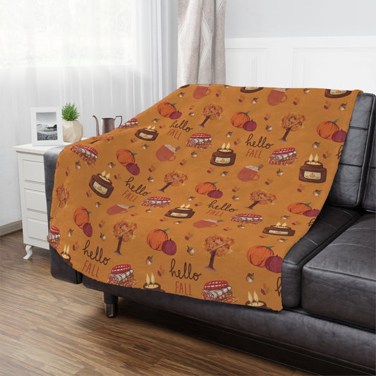 Orange fall-themed minky blanket with pumpkins, apples, and 'hello fall' text draped over a gray sofa.