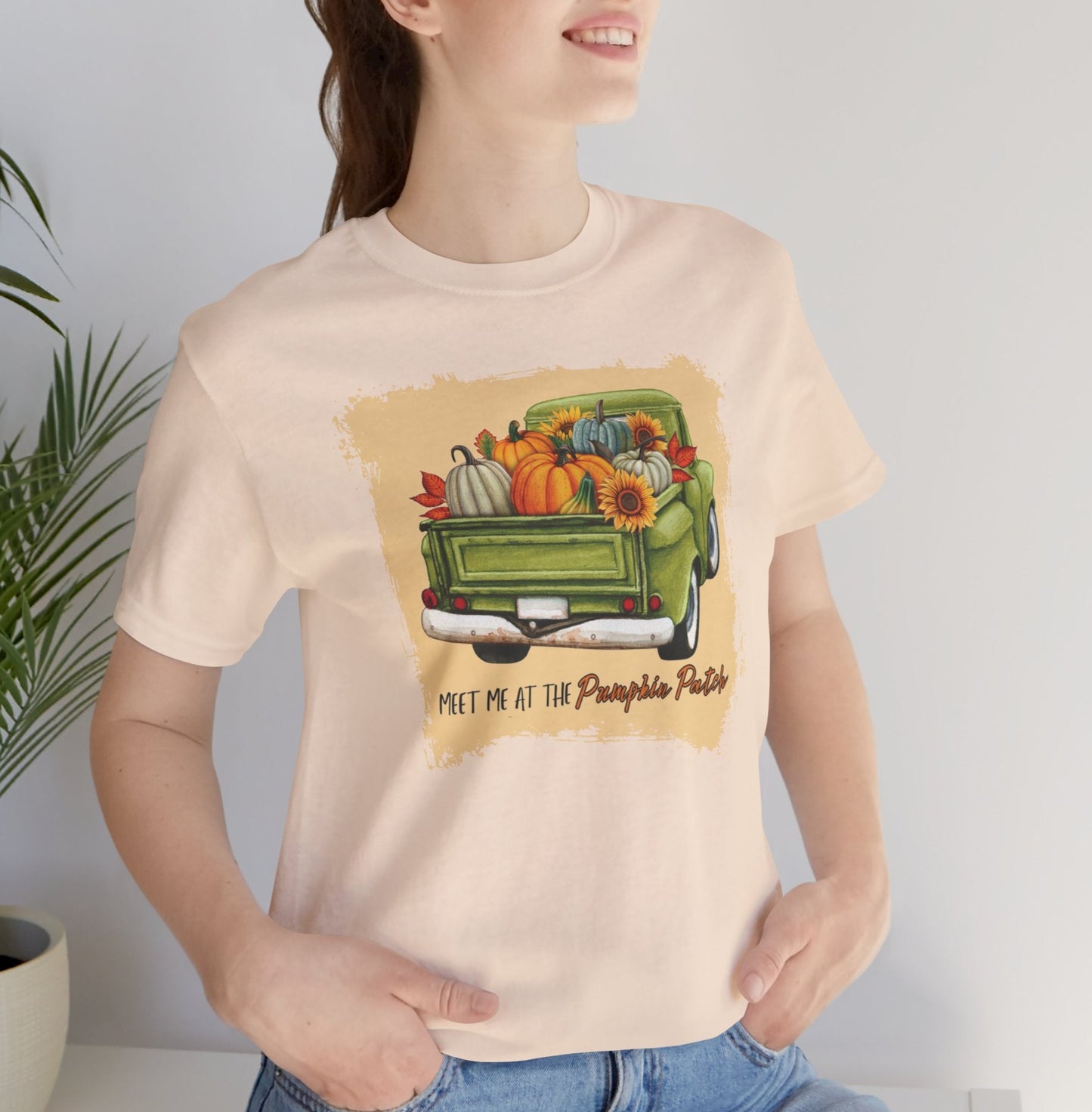 Person wearing a cream t-shirt with a graphic of a truck filled with pumpkins and fall decorations.