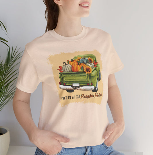 Person wearing a cream t-shirt with a graphic of a truck filled with pumpkins and fall decorations.