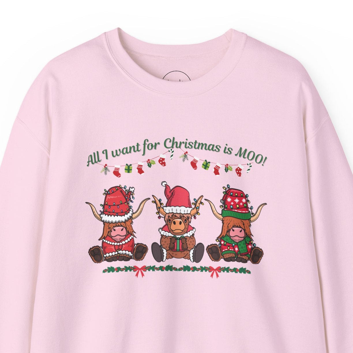 A pink sweatshirt with "All I Want for Christmas Is MOO" sweatshirt featuring three festive cows wearing Santa hats and scarves, printed on cozy crewneck sweaters in white and pink. Exclusive Joyful Verse design by Sara.