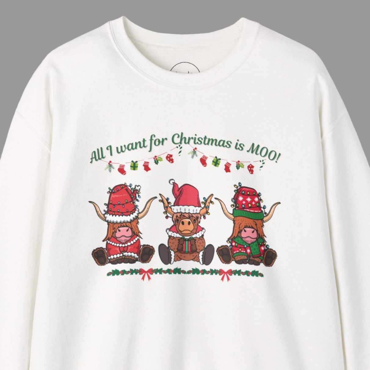 A white sweatshirt with "All I Want for Christmas Is MOO" sweatshirt featuring three festive cows wearing Santa hats and scarves, printed on cozy crewneck sweaters in white and pink. Exclusive Joyful Verse design by Sara.