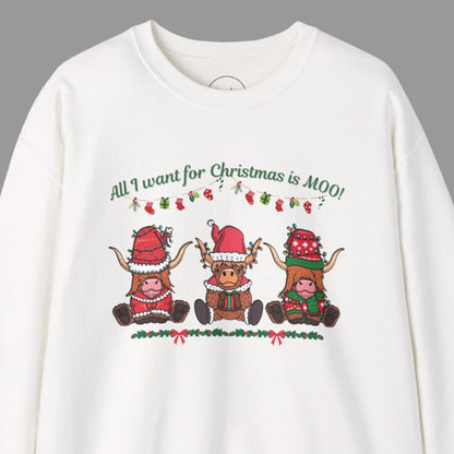 A white sweatshirt with "All I Want for Christmas Is MOO" sweatshirt featuring three festive cows wearing Santa hats and scarves, printed on cozy crewneck sweaters in white and pink. Exclusive Joyful Verse design by Sara.