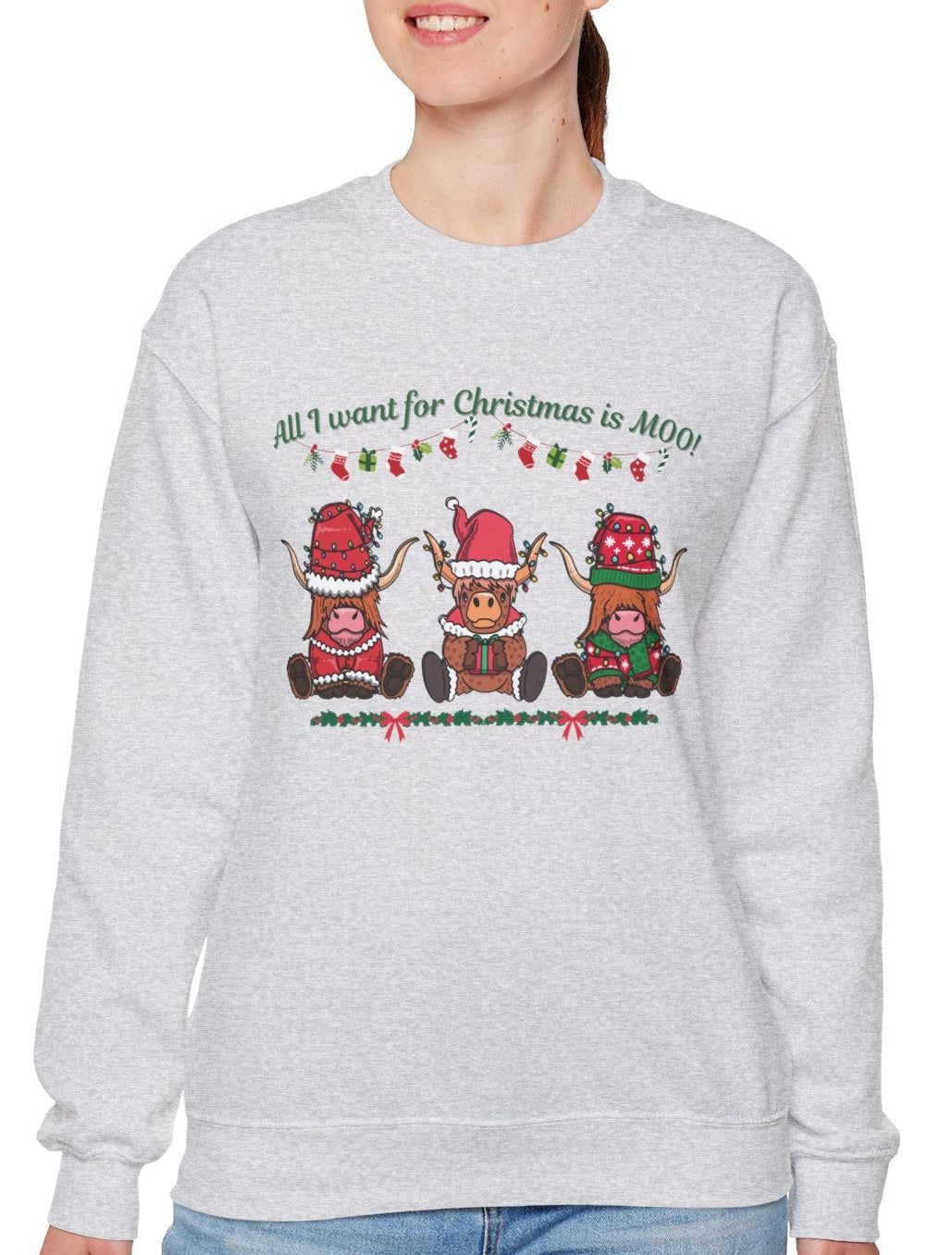 Woman wearing a gray sweatshirt with "All I Want for Christmas Is MOO" sweatshirt featuring three festive cows wearing Santa hats and scarves, printed on cozy crewneck sweaters in white and pink. Exclusive Joyful Verse design by Sara.