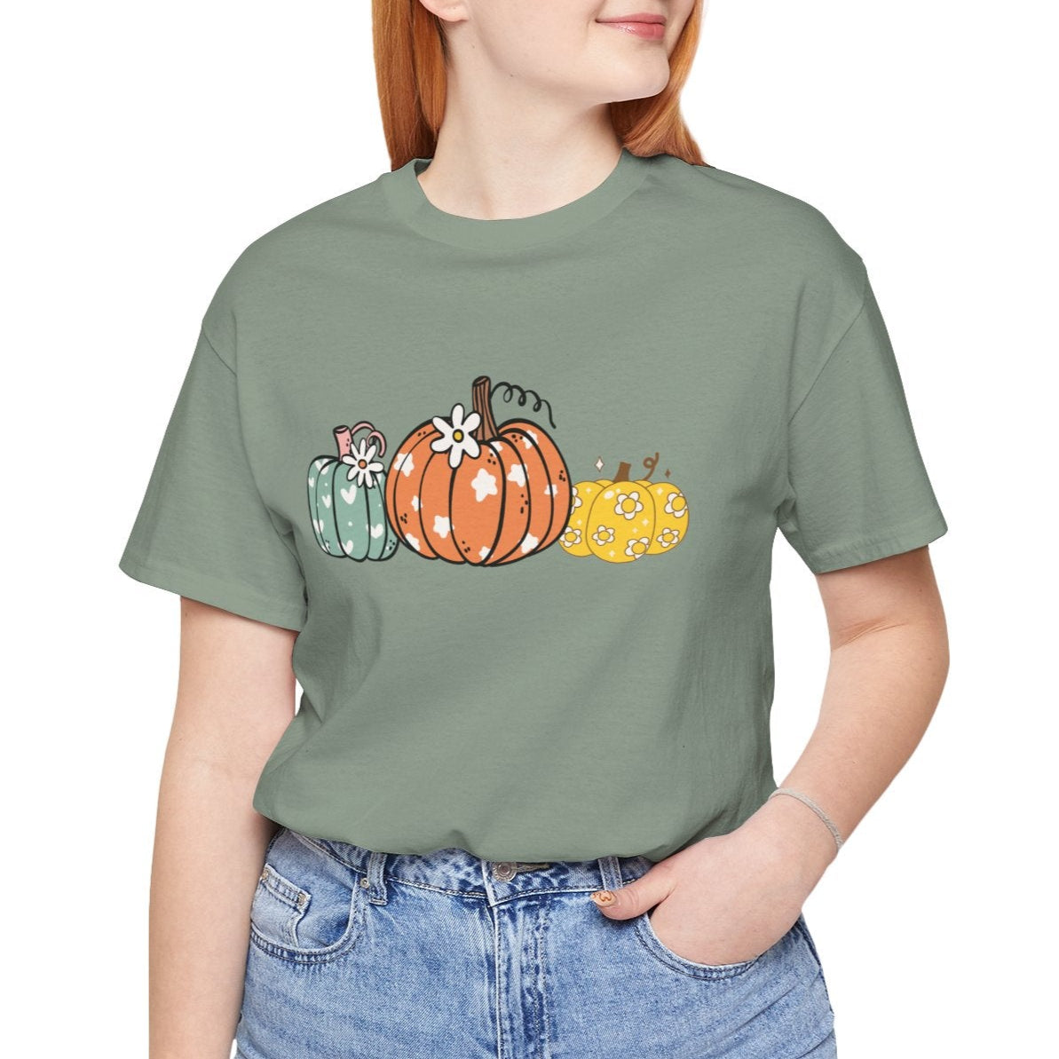 Person wearing a green t-shirt with pumpkins and blue jeans on a white background