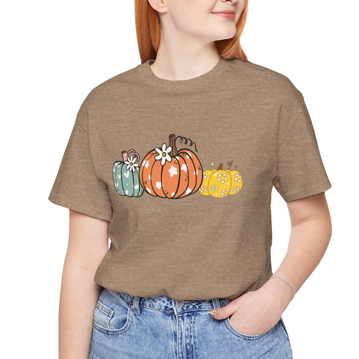 Person wearing a brown t-shirt with colorful pumpkins and blue jeans on a white background
