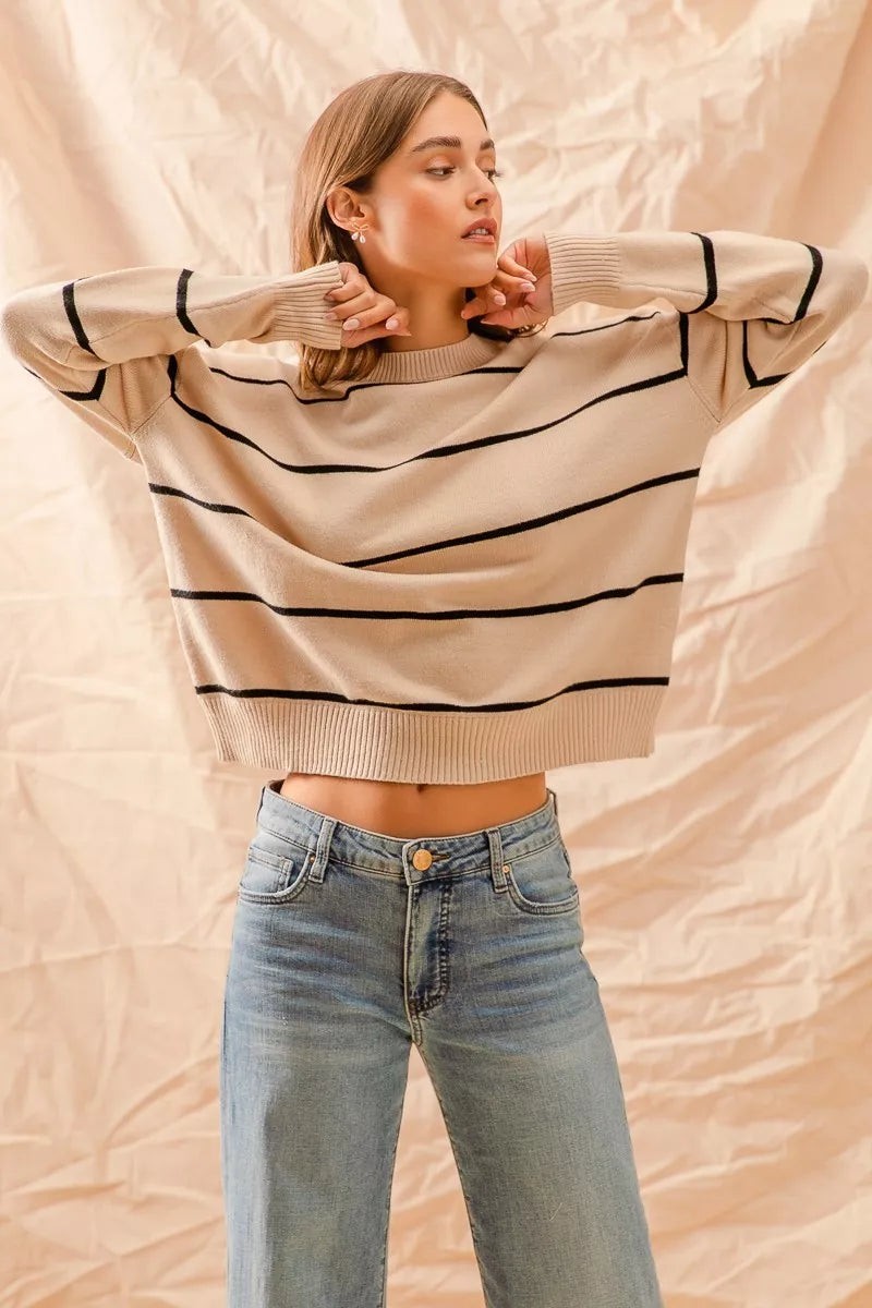 Woman wearing a beige sweater with black stripes and blue jeans against a beige background