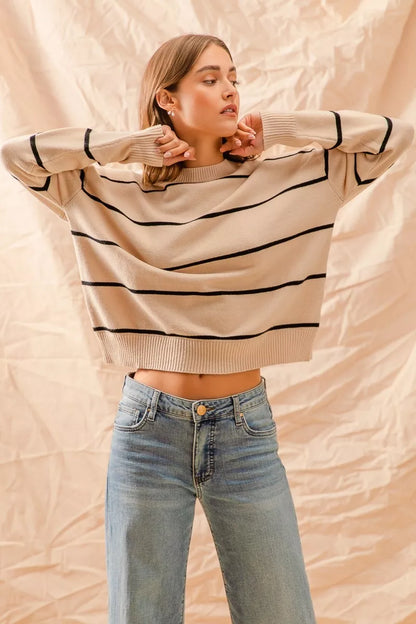 Woman wearing a beige sweater with black stripes and blue jeans against a beige background
