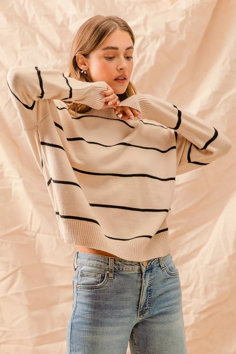 Woman wearing a cream sweater with black stripes and blue jeans against a beige background