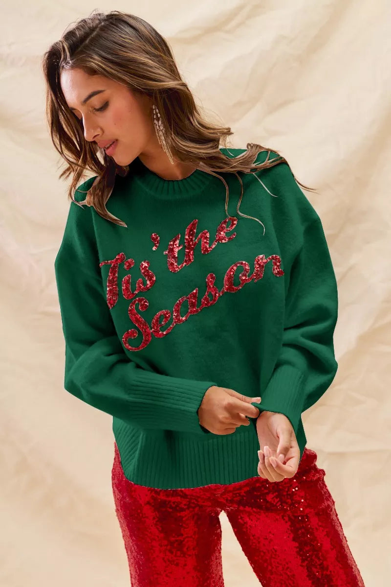Woman wearing a green sweater with 'Tis the Season' red sequins text on a gray background